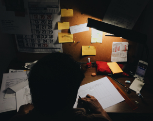 A chalkboard sign hanging on a post. The sign says in white chalk "Welcome please come in".